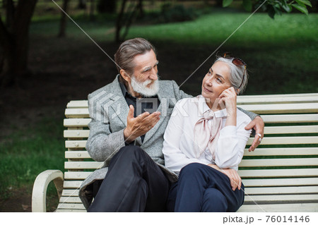 Romantic aged couple sitting on wooden bench at green park Romantic aged couple sitting on wooden bench at green park 76014146
