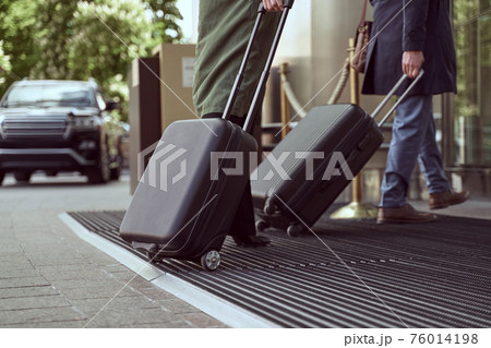 Joyful man in a cloak and his elegant wife arriving at a hotel with their luggage 76014198