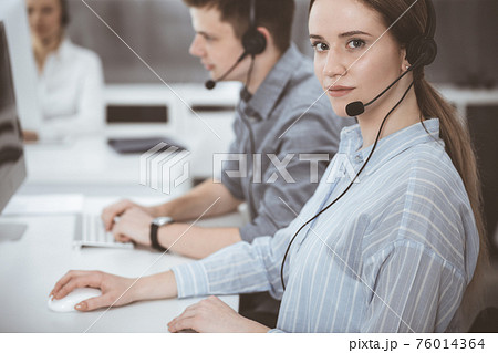 Call center. Group of casual dressed operators at work. Brunette business woman in headset at customer service office 76014364