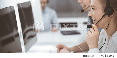 Call center. Group of casual dressed operators at work. Blond business woman in headset at customer service office. Telesales in business Call center. Group of casual dressed operators at work. Blond business woman in headset at customer service office. Telesales in business 76014365