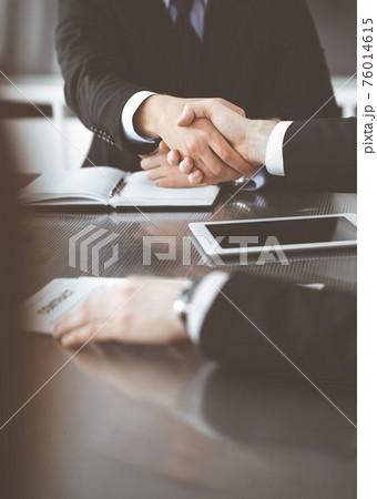 Unknown businessmen shaking hands above the glass desk in a modern office, close-up. Unknown business people at meeting. Teamwork, partnership and handshake concept Unknown businessmen shaking hands above the glass desk in a modern office, close-up. Unknown business people at meeting. Teamwork, partnership and handshake concept 76014615