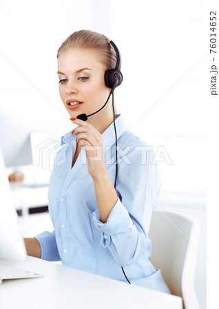 Blond woman call operator is using computer and headset for consulting clients online. Group of diverse people working as customer service occupation. Business concept Blond woman call operator is using computer and headset for consulting clients online. Group of diverse people working as customer service occupation. Business concept 76014652