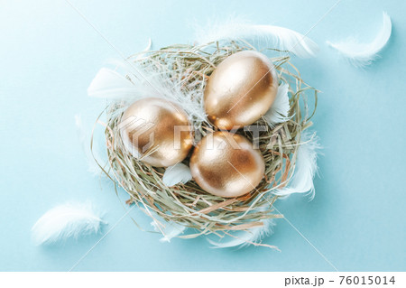 Easter Golden eggs in basket with white feathers on pastel blue background in Happy Easter decoration. Spring holiday flat lay concept. Easter Golden eggs in basket with white feathers on pastel blue background in Happy Easter decoration. Spring holiday flat lay concept. 76015014