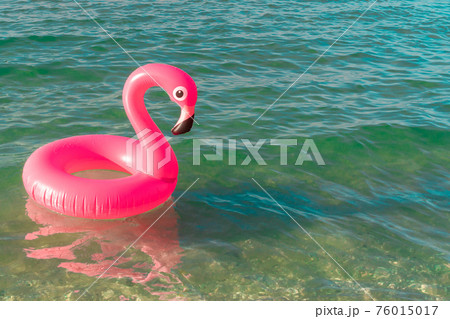 Sea background. Pink inflatable flamingo in blue ocean water for sea summer beach background. Luxury lifestyle travel. Sea background. Pink inflatable flamingo in blue ocean water for sea summer beach background. Luxury lifestyle travel. 76015017