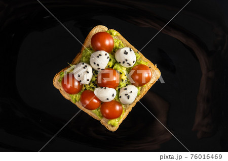 A cheese and tomato sandwich sits in a black plate on a wooden background A cheese and tomato sandwich sits in a black plate on a wooden background 76016469