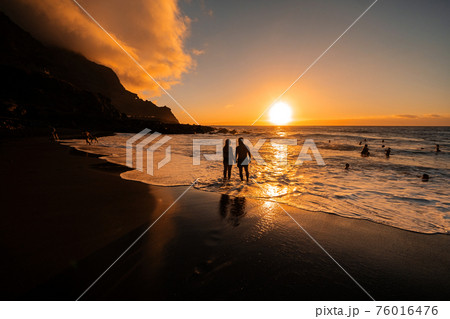 A couple in love stands in the ocean in the evening looking at the beautiful sunset on the island of Tenerife.Spain A couple in love stands in the ocean in the evening looking at the beautiful sunset on the island of Tenerife.Spain 76016476