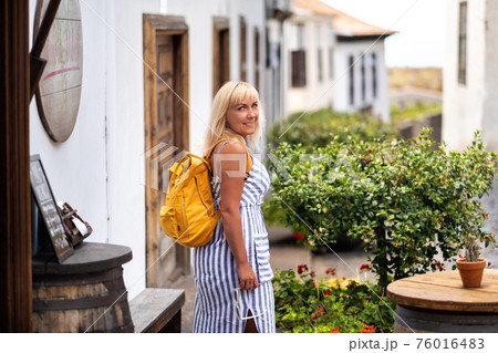 a blonde in a sundress with a backpack walks along the street of the Old town of Garachico on the island of Tenerife.Spain, Canary Islands. 76016483