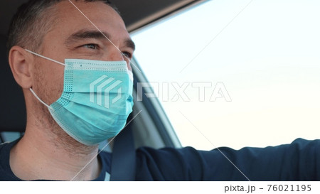 worker driver in mask in the coronavirus a pandemic. delivery service. delivery of travel goods concept. man driver in a protective mask rides a car on the road. food delivery service worker worker driver in mask in the coronavirus a pandemic. delivery service. delivery of travel goods concept. man driver in a protective mask rides a car on the road. food delivery service worker 76021195