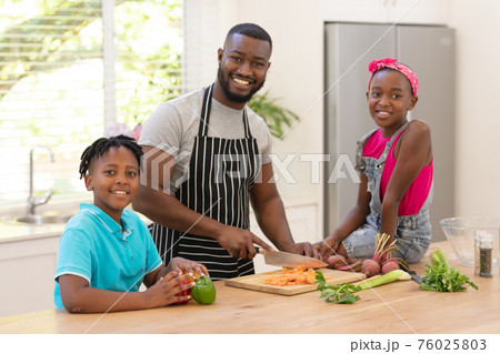 Happy african american father teaching daughter and son cooking in the kitchen 76025803