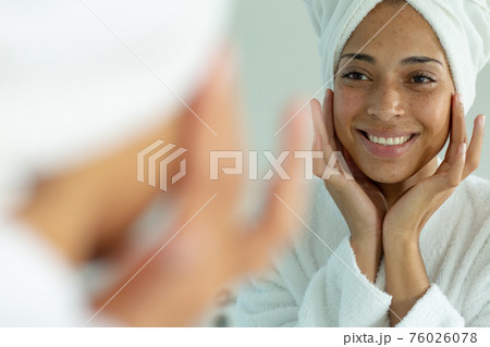 Mixed race woman wearing bathrobe and cleansing face mask in bathroom 76026078