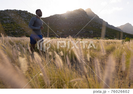 Fit african american man in sportswear running through tall grass 76026602