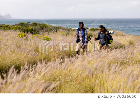 Fit afrcan american couple wearing backpacks nordic walking with poles in mountain countryside 76026650