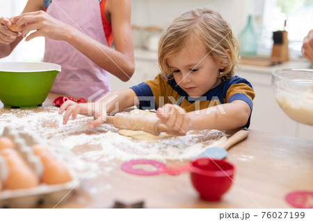 Caucasian boy in kitchen rolling dough with sister, wearing aprons baking cookies together Caucasian boy in kitchen rolling dough with sister, wearing aprons baking cookies together 76027199