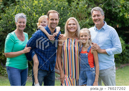 Portrait of caucasian parents, grandparents and grandchildren standing in garden smiling to camera 76027202