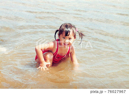 昔のフィルム写真　海で遊ぶ二つ結びの女の子 76027967