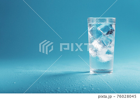 A glass with ice water and ice cubes on a blue background. 76028045