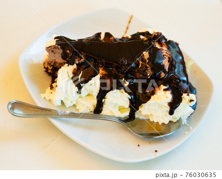 Slice of tasty chocolate cake served on white plate with whipped cream Slice of tasty chocolate cake served on white plate with whipped cream 76030635