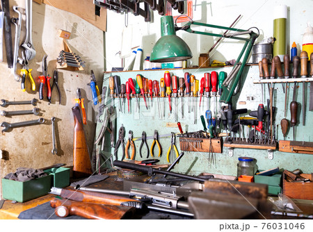 Workplace of gunsmith in weapons workshop with tools and disassembled shotgun 76031046