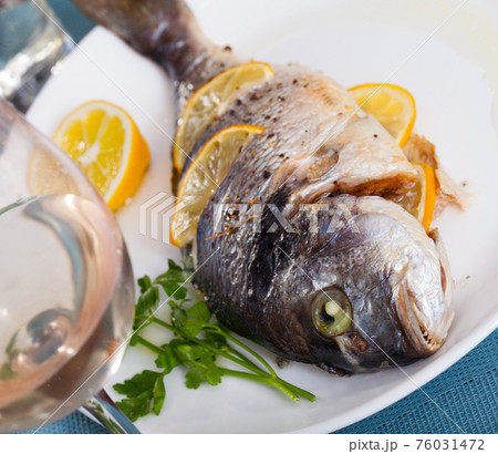 Top view of whole grilled dorada served with lemon and greens at plate 76031472