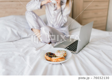 Young woman in white towel and robe in kitchen during quarantine. Hold donut on plate. 76032130