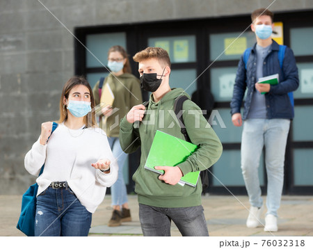 Young girl and guy in protective masks walk along street holding hands 76032318