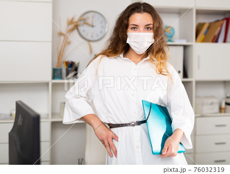 Business woman in face mask standing in white office 76032319