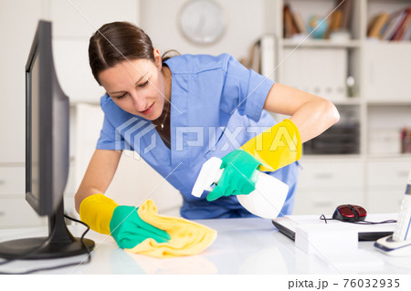 Cleaning lady of cleaning company wipes dust from table in office Cleaning lady of cleaning company wipes dust from table in office 76032935
