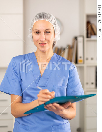 Positive woman doctor in formal wear standing with folder Positive woman doctor in formal wear standing with folder 76032941