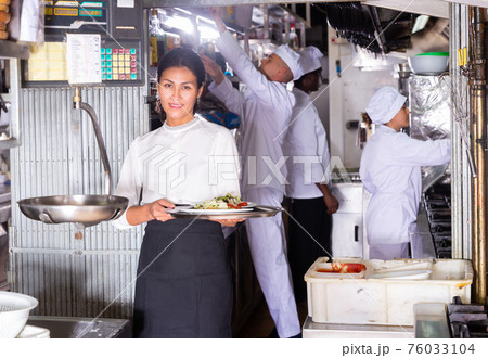 Smiling waitress with ordered dishes in kitchen of restaurant Smiling waitress with ordered dishes in kitchen of restaurant 76033104