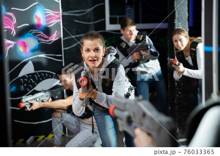 Portrait of excited woman holding laser gun in arena, playing laser tag game with friends 76033365