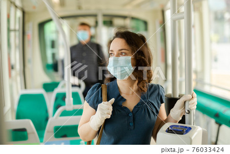 Female in medical mask holding on handrails in bus 76033424
