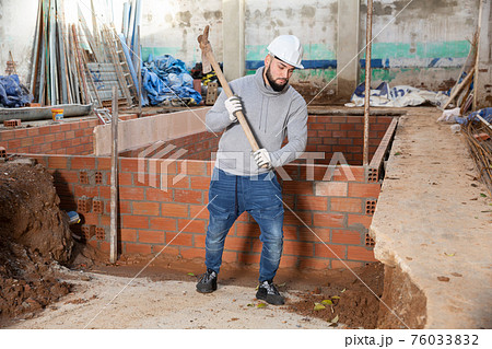 Guy excavating ground with mattock at building site 76033832