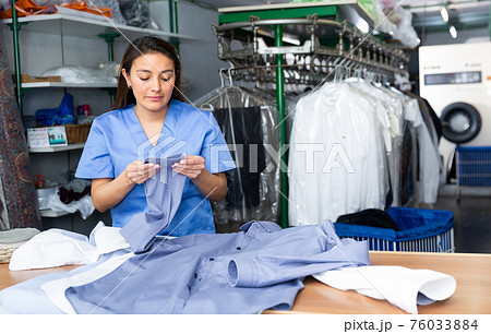 Focused woman dry-cleaning worker checking clean clothes Focused woman dry-cleaning worker checking clean clothes 76033884