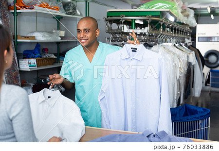 Male employee with client in modern laundry, returning clothing after cleaning Male employee with client in modern laundry, returning clothing after cleaning 76033886