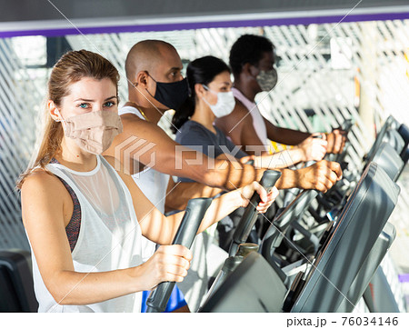 Slim athletic people in protective masks running on treadmill in fitness club Slim athletic people in protective masks running on treadmill in fitness club 76034146