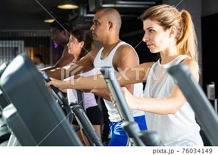 Athletic people running on elliptical trainer in fitness club Athletic people running on elliptical trainer in fitness club 76034149