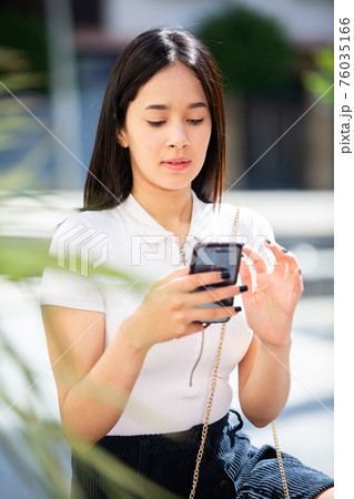 Young positive girl chatting on phone in the city center Young positive girl chatting on phone in the city center 76035166