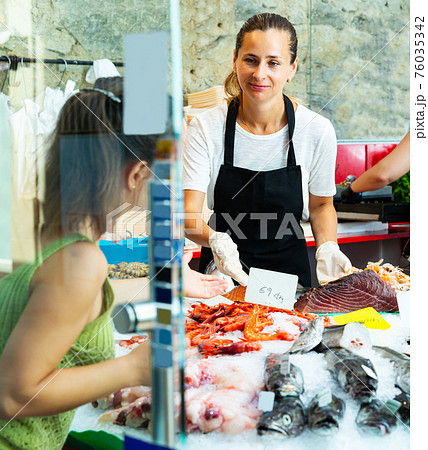 female fishmonger showing variety of fresh fish and seafoods 76035342