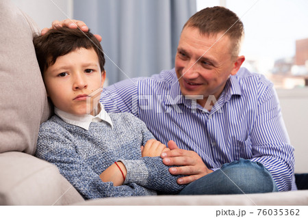 Young father consoling preteen son sitting at sofa after quarrel 76035362