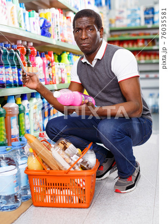 Positive Afro man choosing goods with list in grocery store 76035581