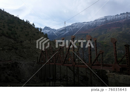 Construction of a new bridge in the Himalayan Mountains in the early cloudy morning. Two people at a height are building a bridge. 76035643
