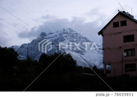 Early cloudy morning in the Himalayan Mountains. Snowy peaks and a pink multi-storey building. 76035651