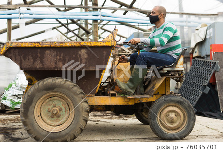 Latin american farmer wearing a protective mask during a pandemic, sits behind the wheel. Latin american farmer wearing a protective mask during a pandemic, sits behind the wheel. 76035701