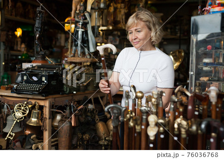 Senior woman chooses rare walking stick at flea market Senior woman chooses rare walking stick at flea market 76036768
