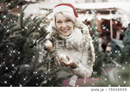 Woman in Christmas hat choosing decorations and Christmas tree Woman in Christmas hat choosing decorations and Christmas tree 76036949