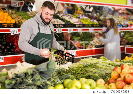 Man in an apron puts onion from the box on the counter 76037103