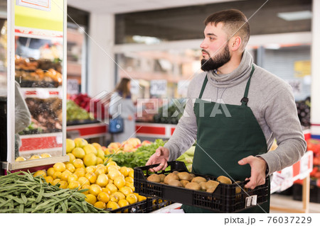 Man seller moving box of kiwi in grocery shop 76037229