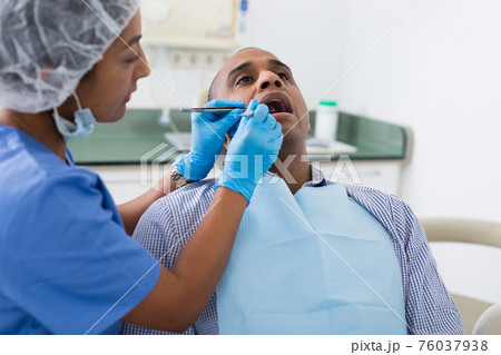 Dentist in uniform is examinating man on chair 76037938