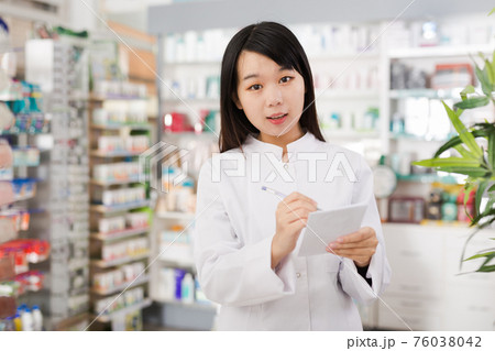 Chinese female looking medicine with notebook near shelves in pharmacy Chinese female looking medicine with notebook near shelves in pharmacy 76038042