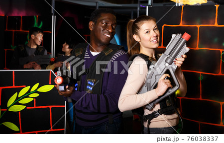 couple standing back to back holding laser guns during lasertag game 76038337